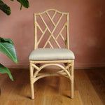 Natural Rattan chippendale style chair with a cream cushion against a pink wall