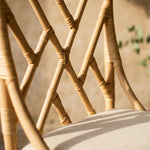 Natural Rattan chippendale style chair with a cream cushion against a pink wall
