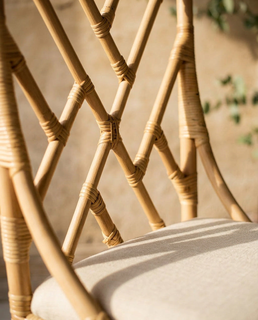 Natural Rattan chippendale style chair with a cream cushion against a pink wall