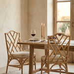 Natural Rattan chippendale style chair with a cream cushion against a pink wall