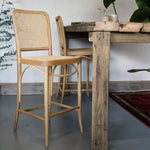 Wooden bar stools with wicker backs in front of a rustic wooden table.