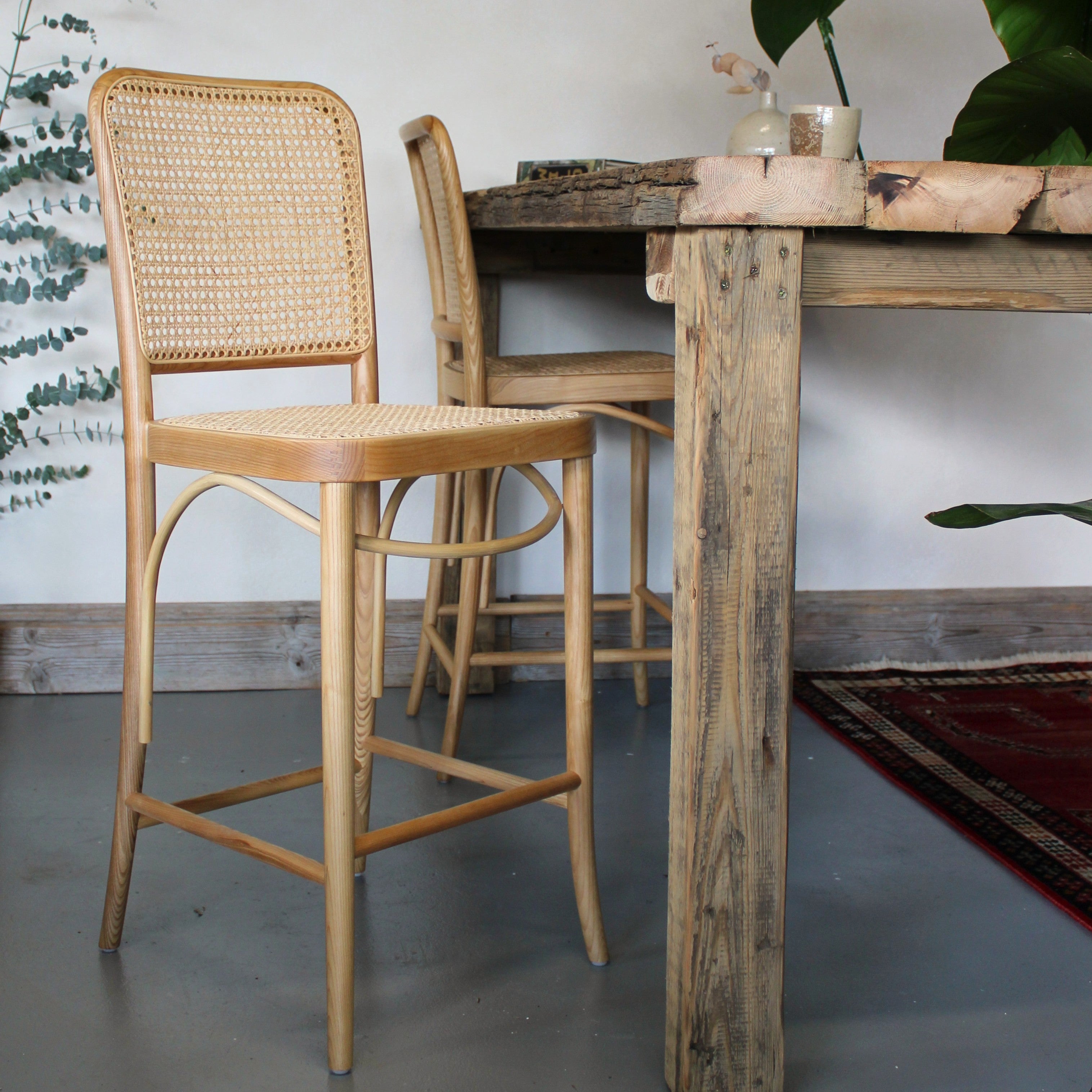 Wooden bar stools with wicker backs in front of a rustic wooden table.