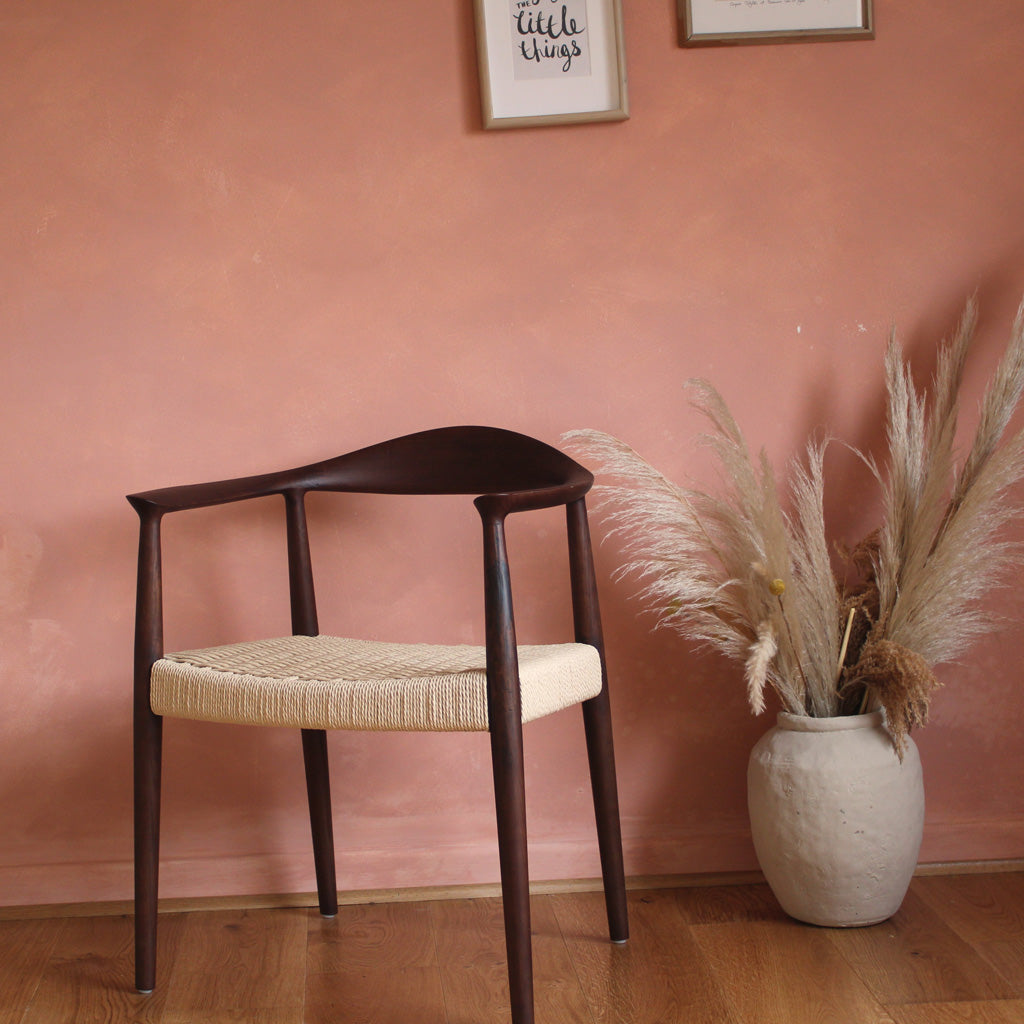 Wooden chair with woven seat in a room with wooden floor and plant- Walnut colour.
