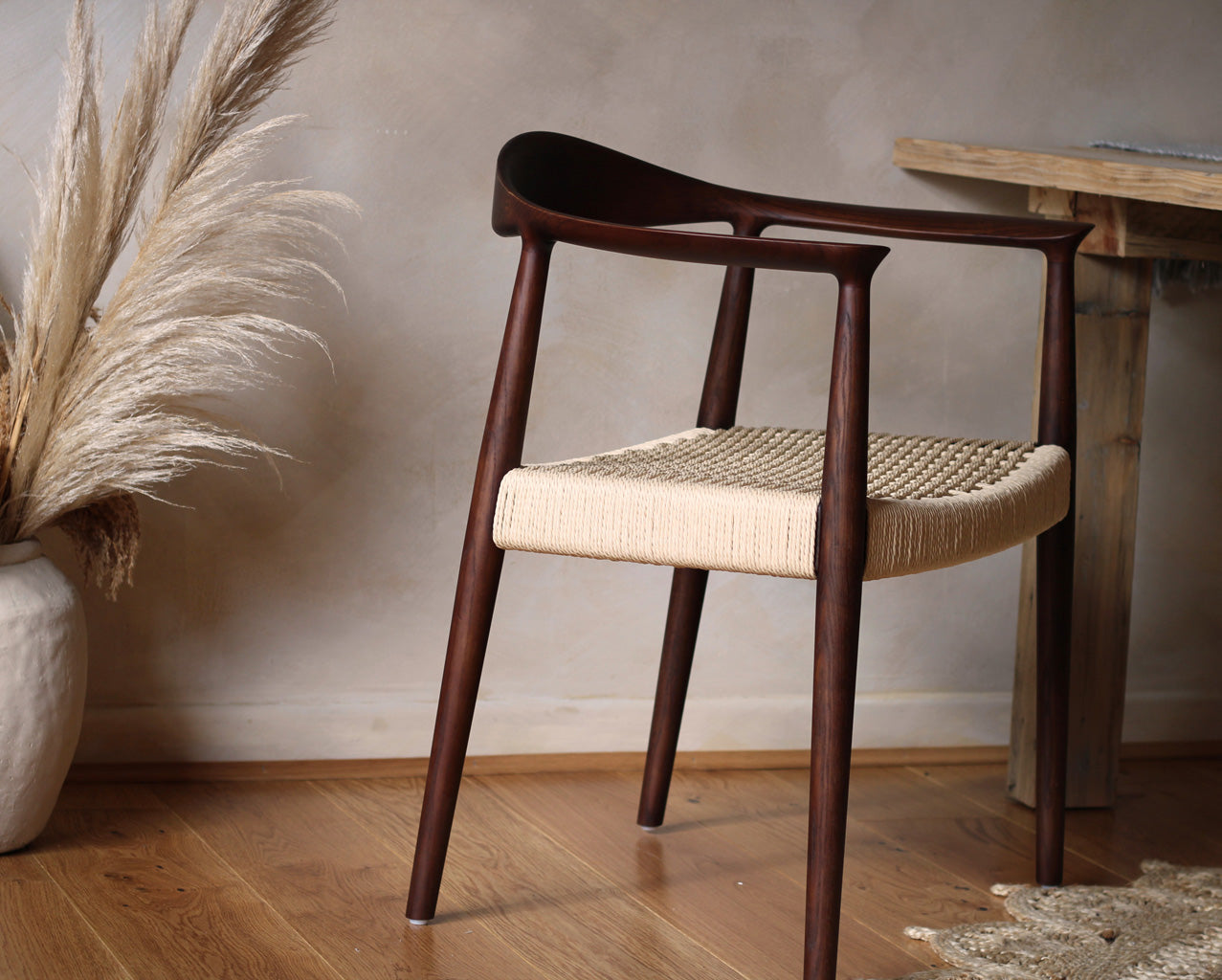 Wooden chair with woven seat in a room with wooden floor and plant- Walnut colour.