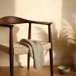 Wooden chair with woven seat in a room with wooden floor and plant- Walnut colour.
