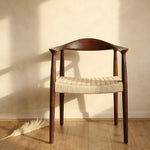 Wooden chair with woven seat in a room with wooden floor and plant- Walnut colour.