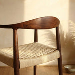 Wooden chair with woven seat in a room with wooden floor and plant- Walnut colour.