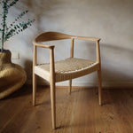 Wooden chair with woven seat in a room with wooden floor and plant.