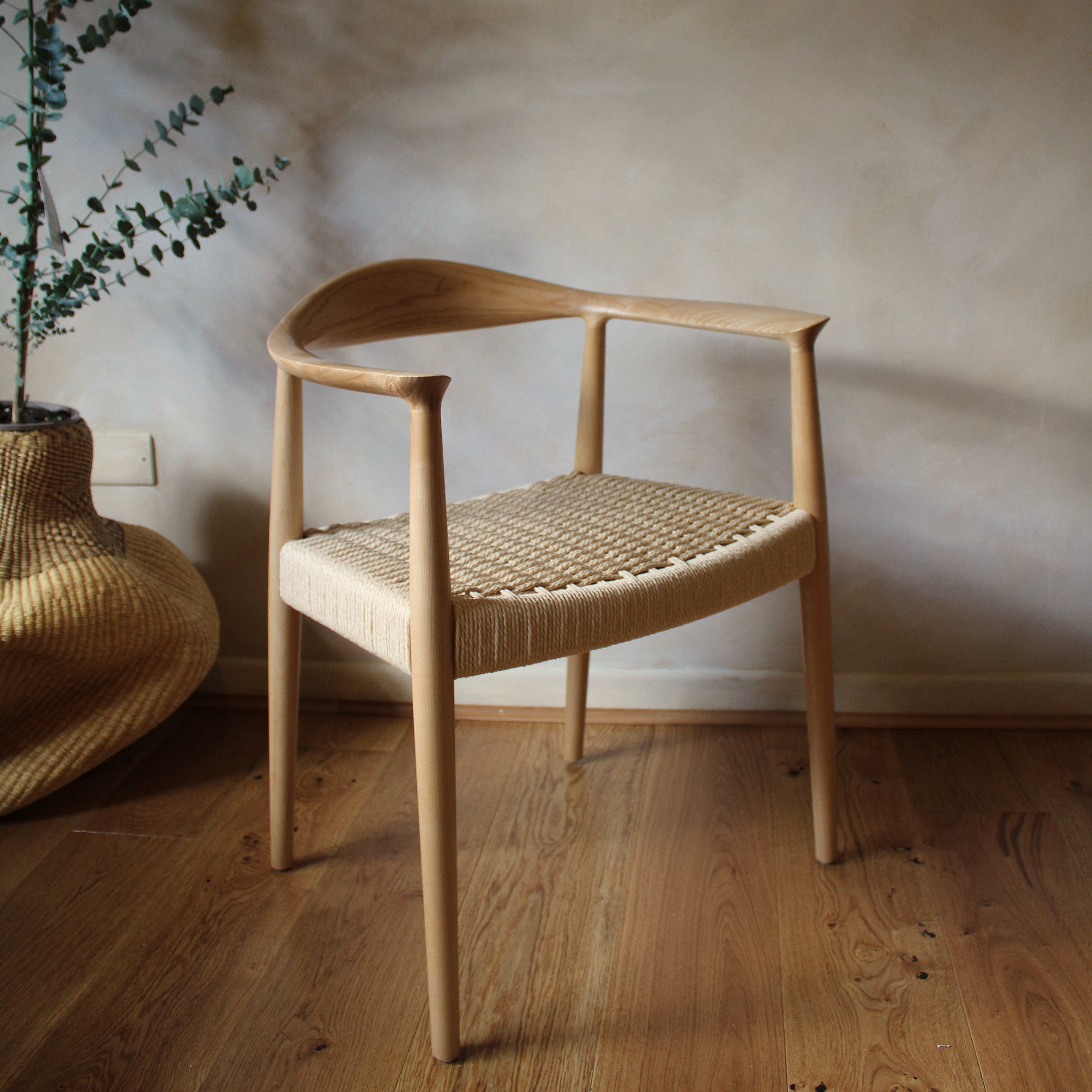 Wooden chair with woven seat in a room with wooden floor and plant.